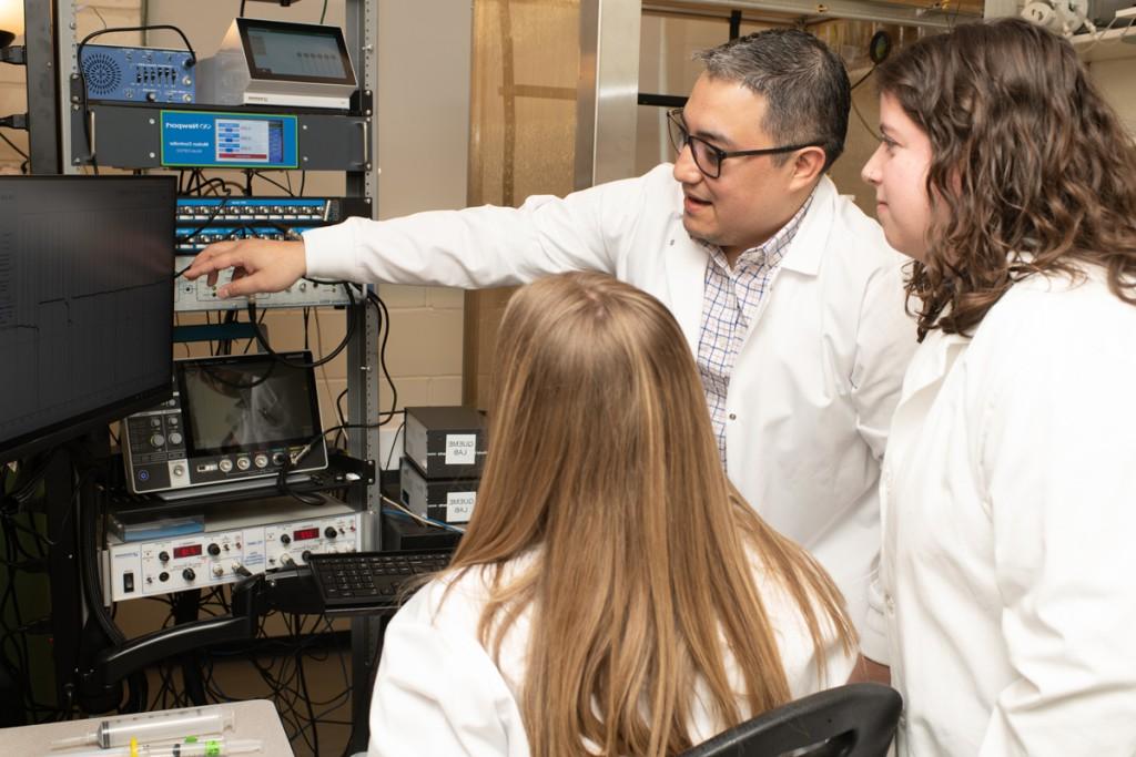 Luis Queme and two students look at a graph on a monitor in his lab